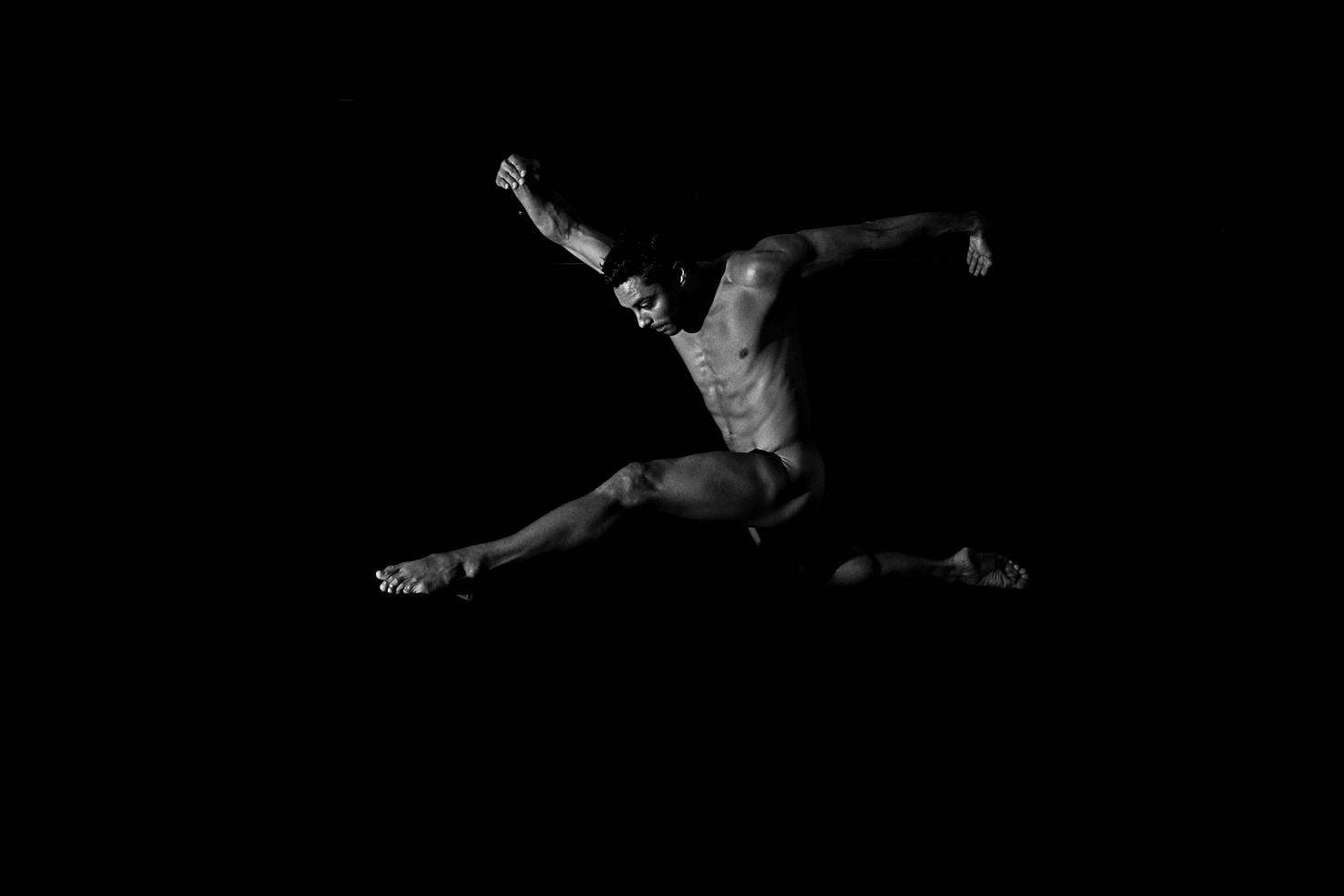 Bailarín desnudo en salto, con un brazo por delante y las piernas extendidas en zancada, sobre fondo negro.