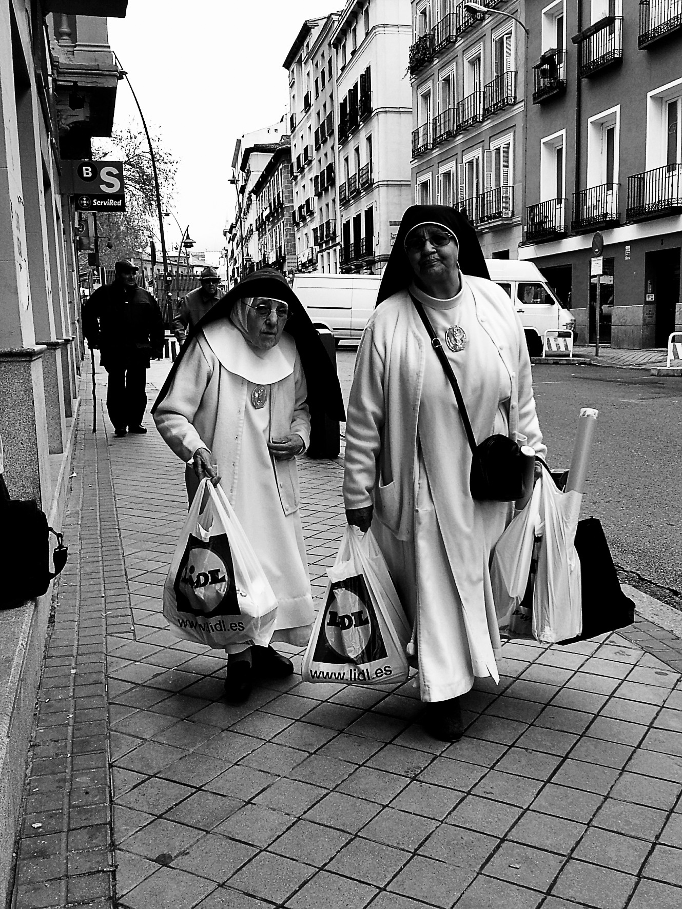 Two nuns in habits walking down a Madrid street carrying shopping bags.