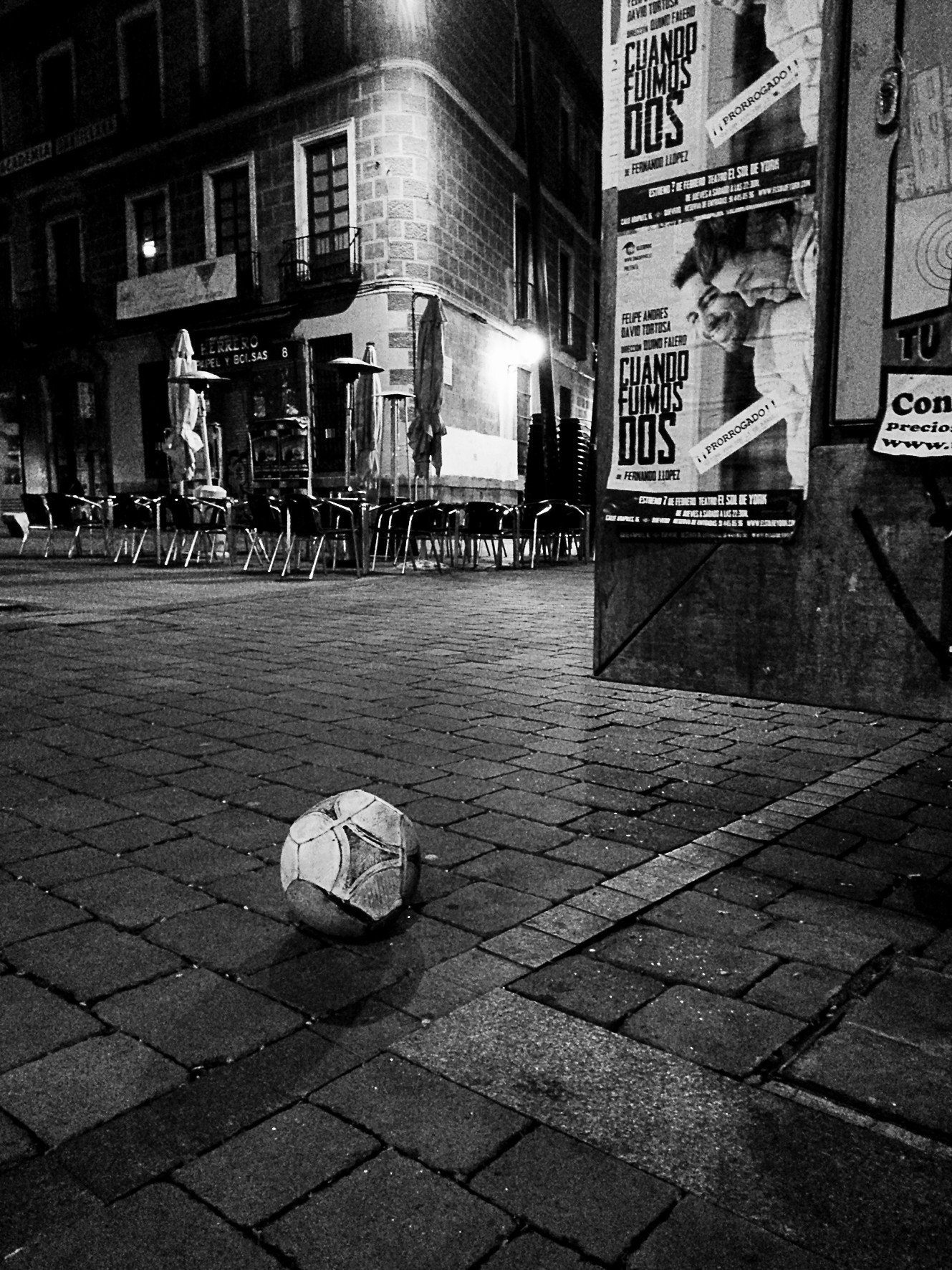 A football resting in the middle of a cobbled square at night, with nobody around.