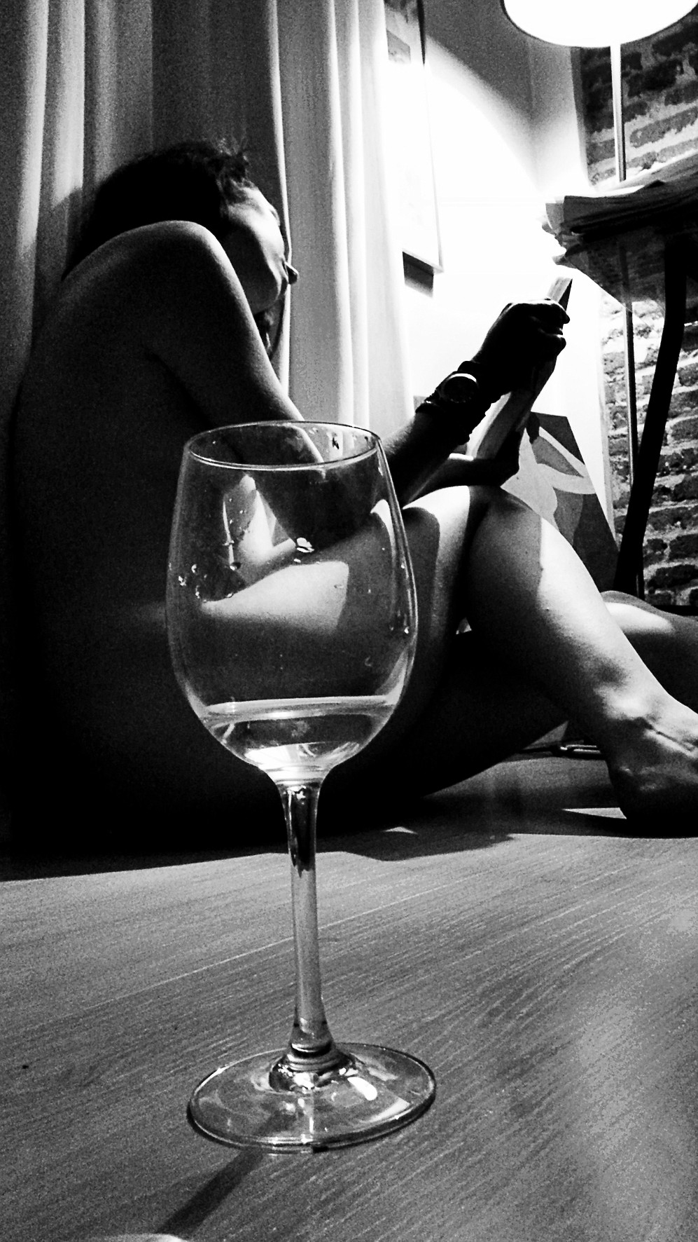 Woman seated on the floor reading a tablet, a wine glass in the foreground.