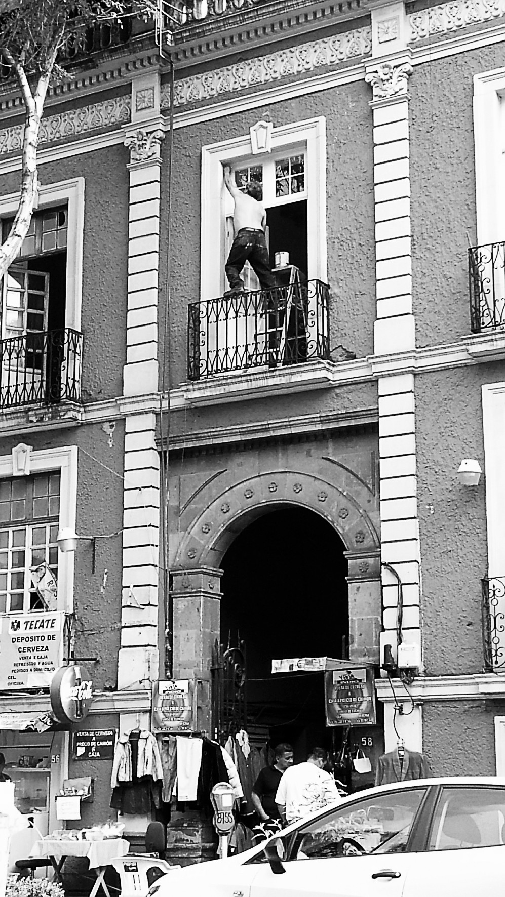 Building facade with a man leaning out of a high window and an arched doorway at street level.