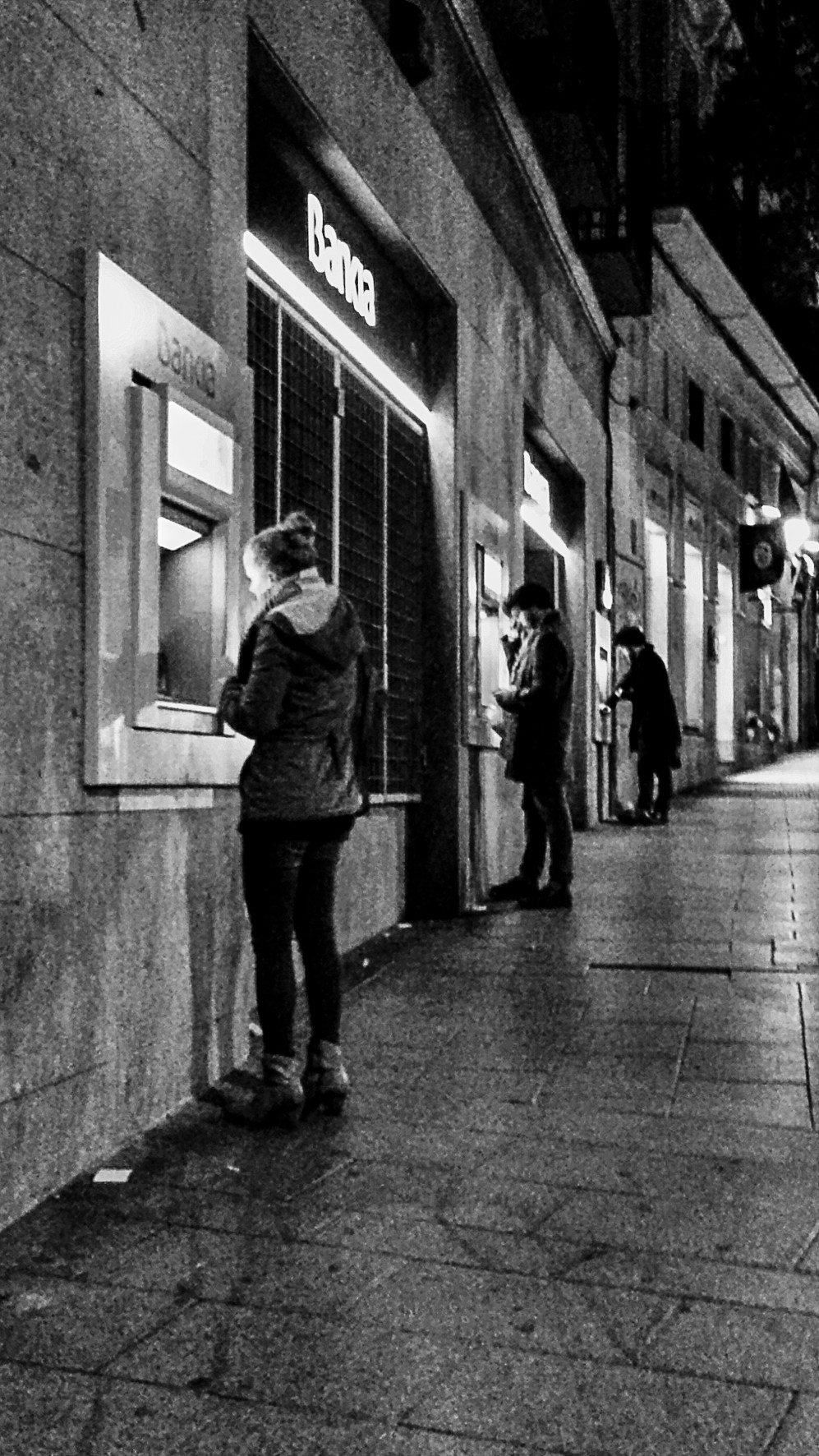 A woman withdrawing cash from an ATM on a narrow street at night.