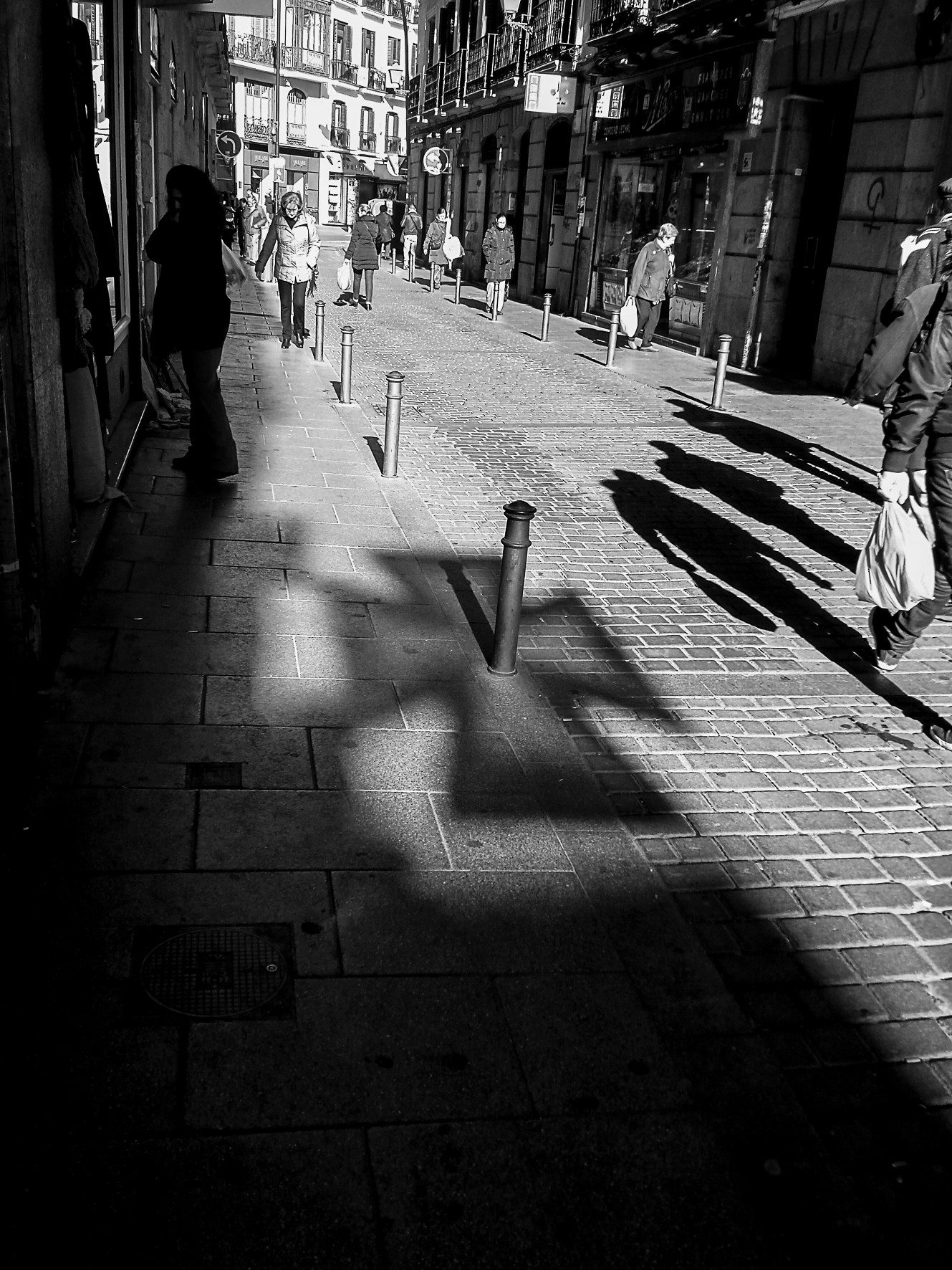 A narrow street with long shadows across the pavement and a man standing in the distance.