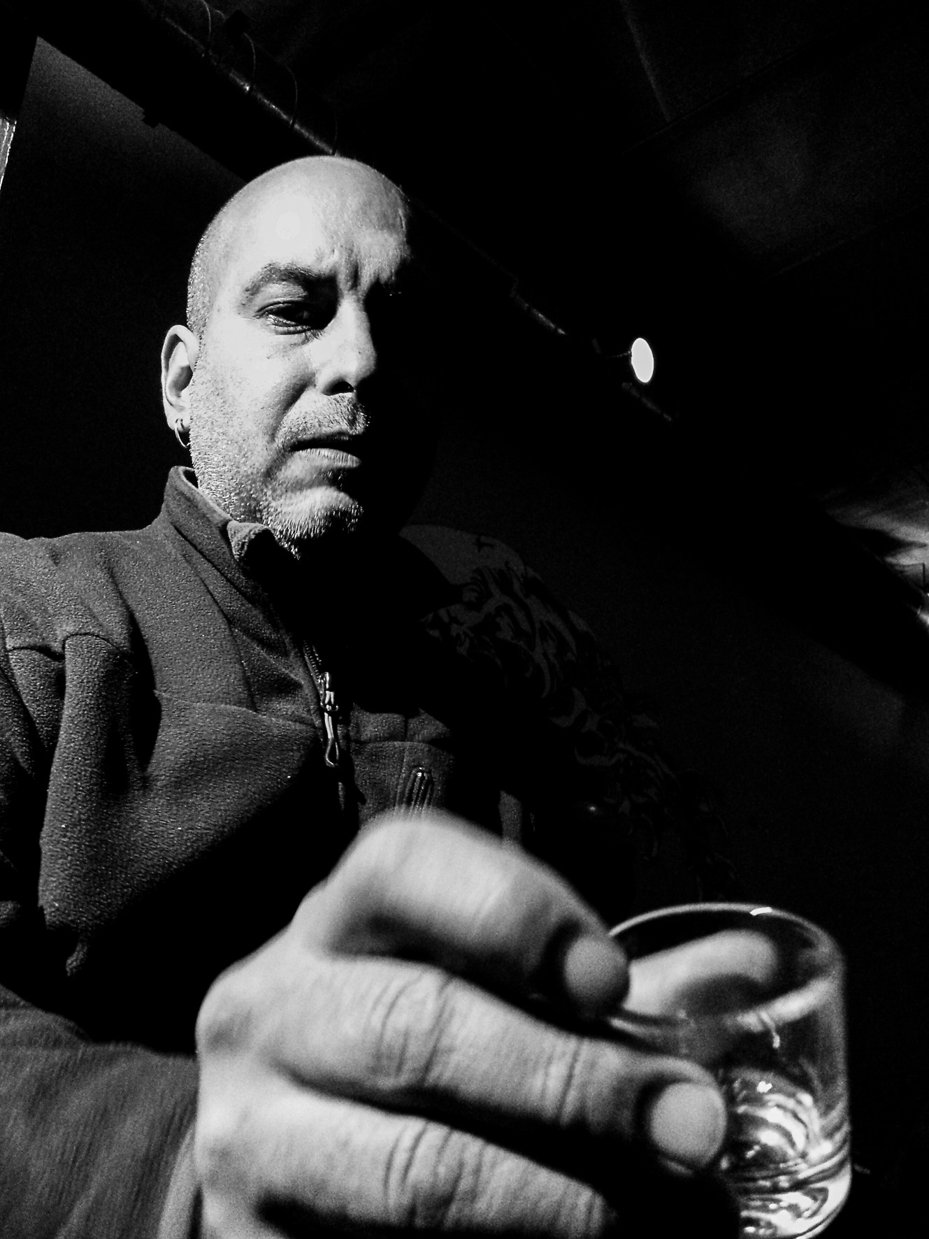 Wide-angle self-portrait of a bald man holding a shot glass in the foreground.