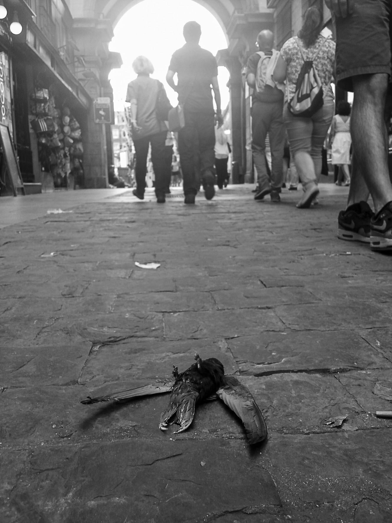 People walking away through an archway toward the light; in the foreground, a dark wing-shaped object on the ground.