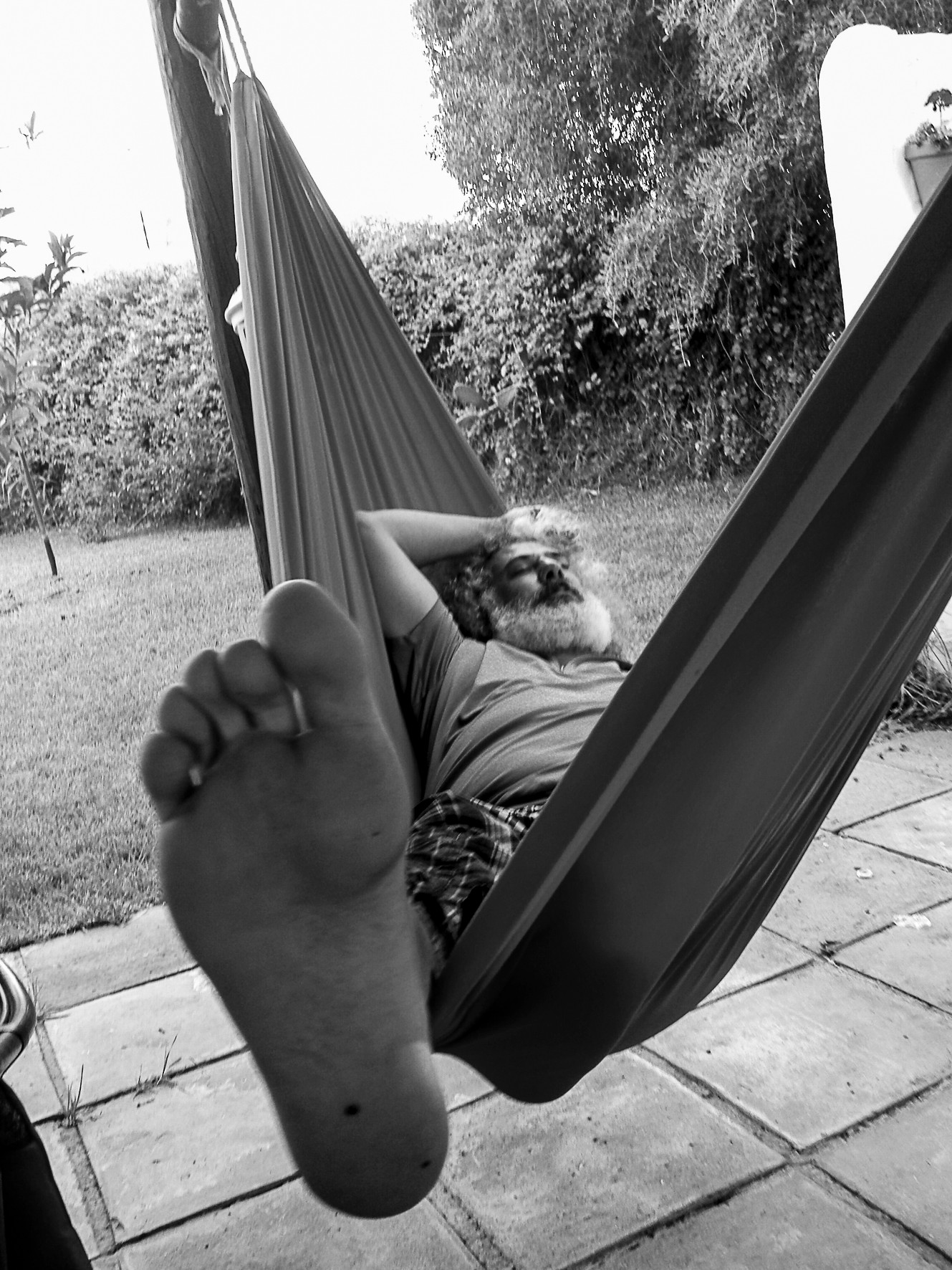 A person in a hammock, seen from the feet, in a garden.