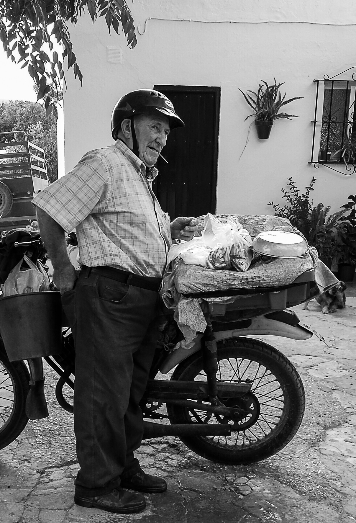 An older man in a helmet beside his motorbike, a basket of food on it, looking to one side.