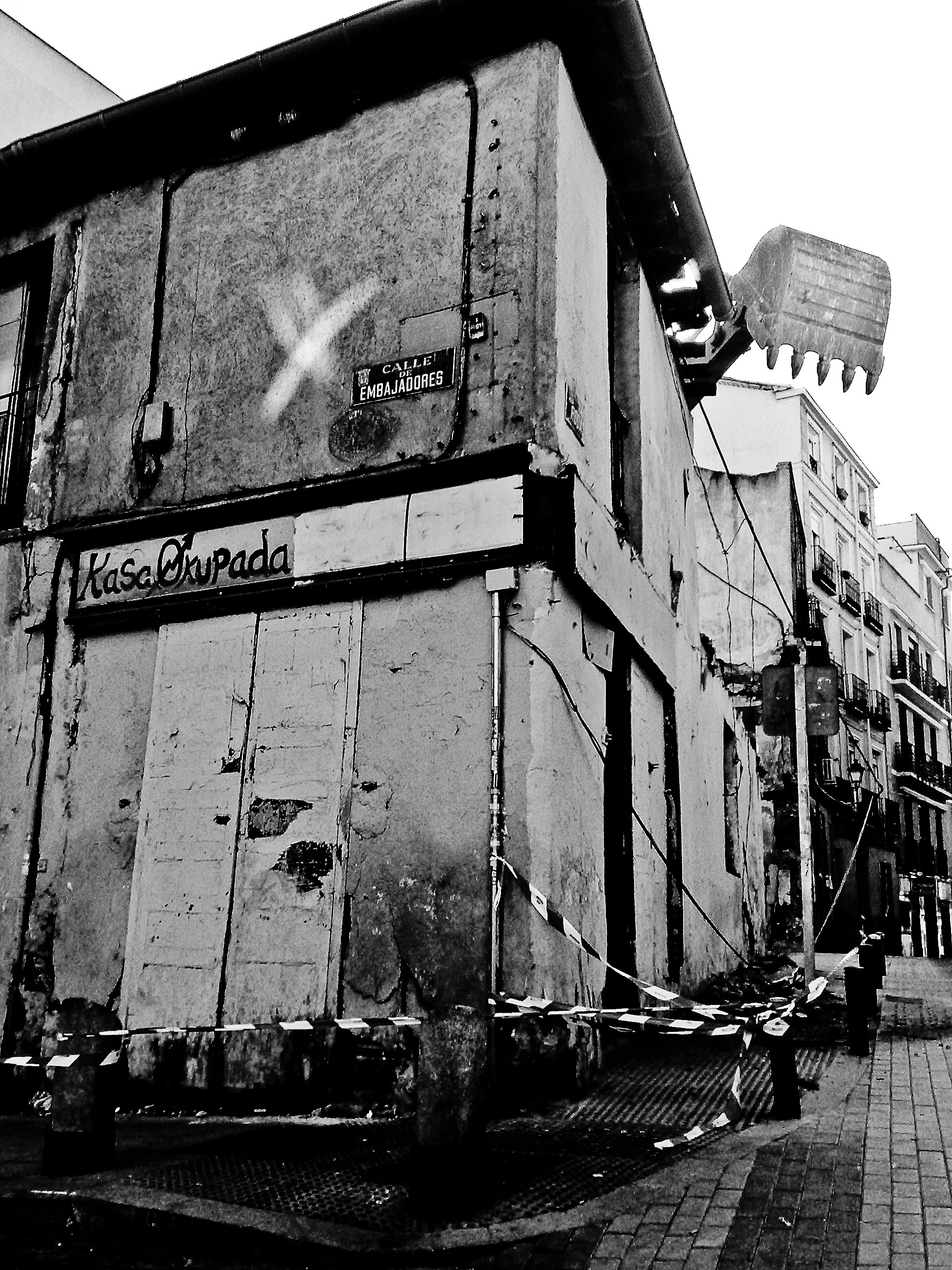 A ruined, taped-off wooden building with an excavator poised to demolish it.