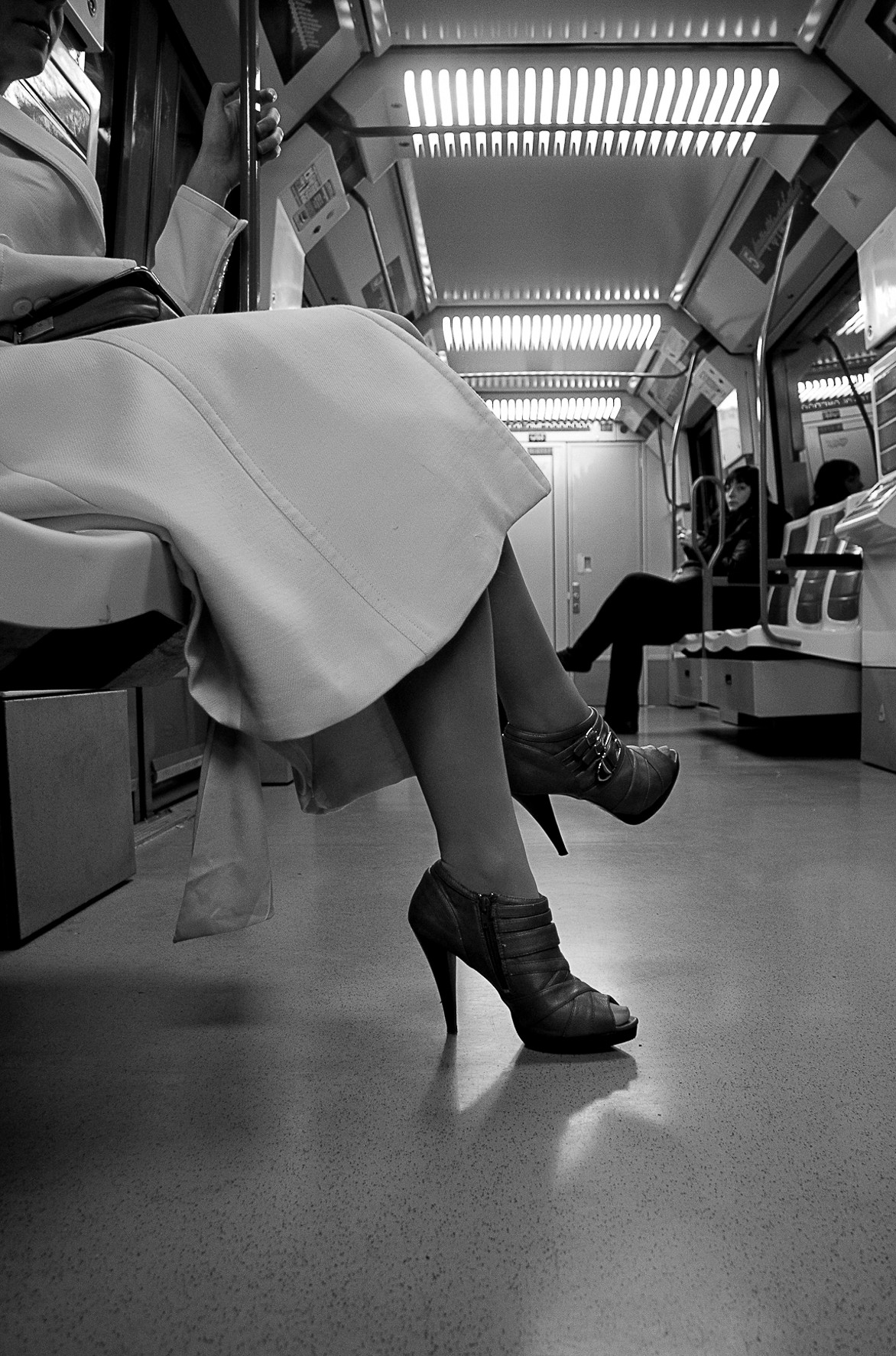 Legs of a woman in a long skirt and ankle boots, seated in a metro carriage.
