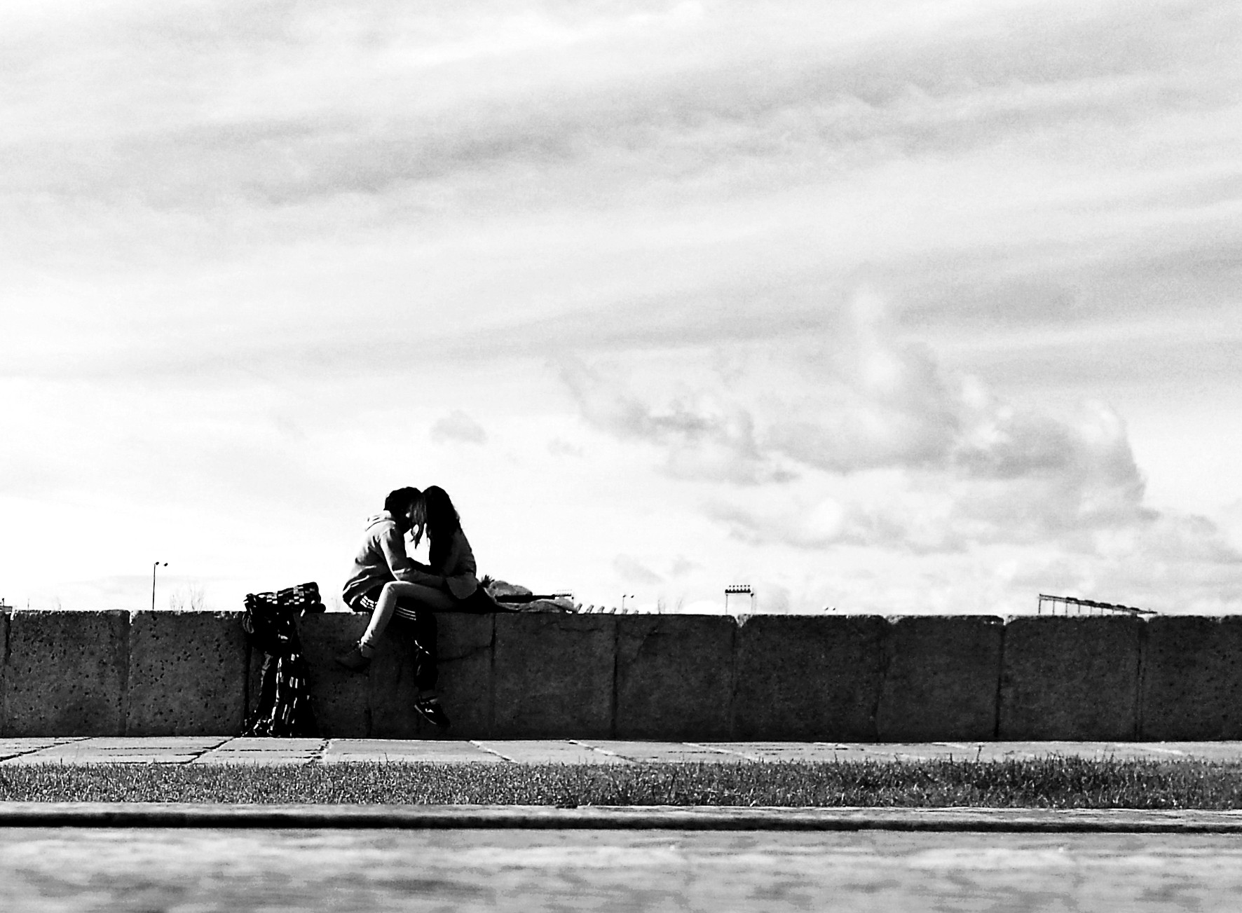 A couple embracing on a wall, silhouetted against a cloudy sky.