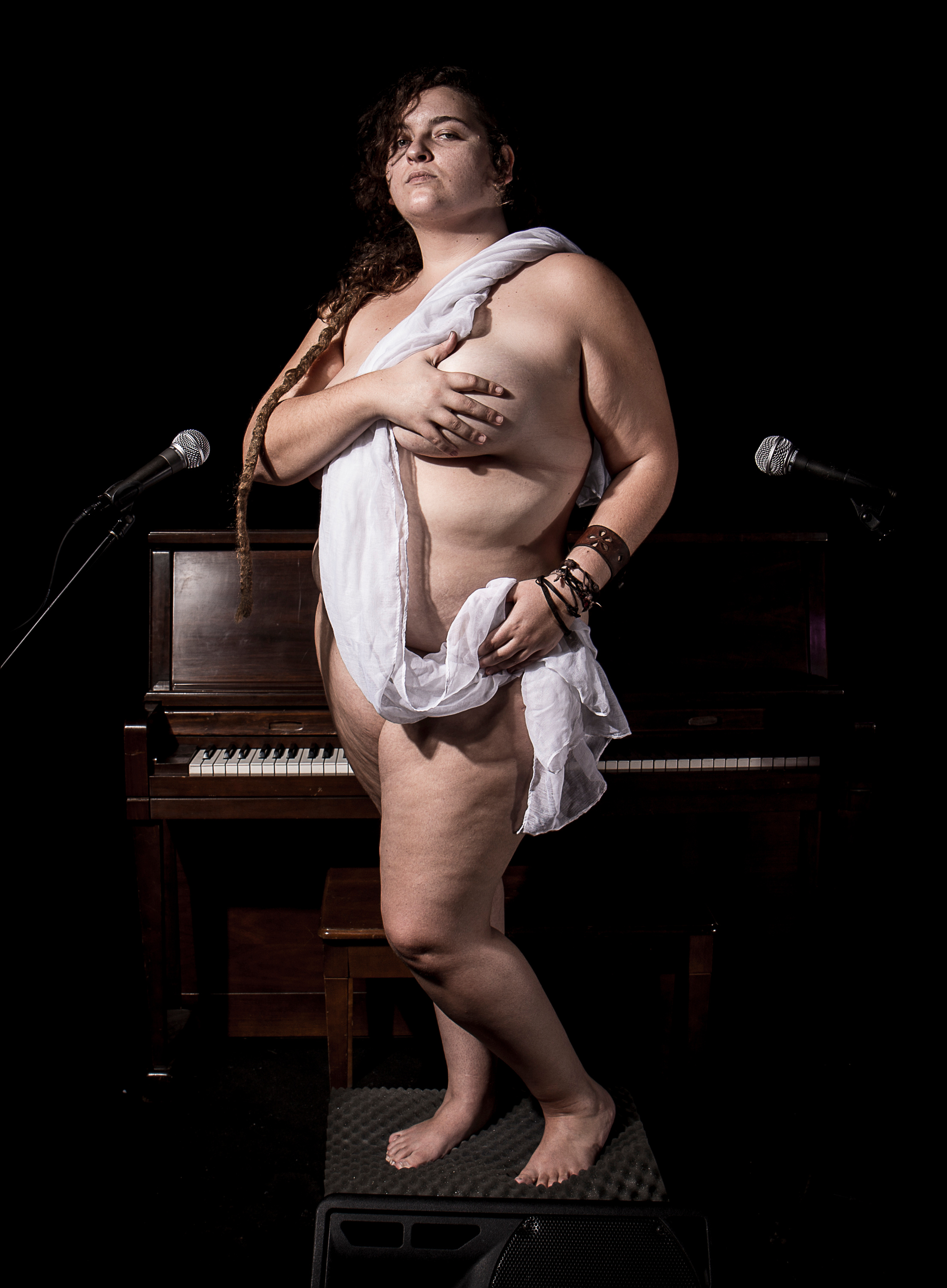 "Venus". A nude woman draped in cloth, standing on a piano among microphones.